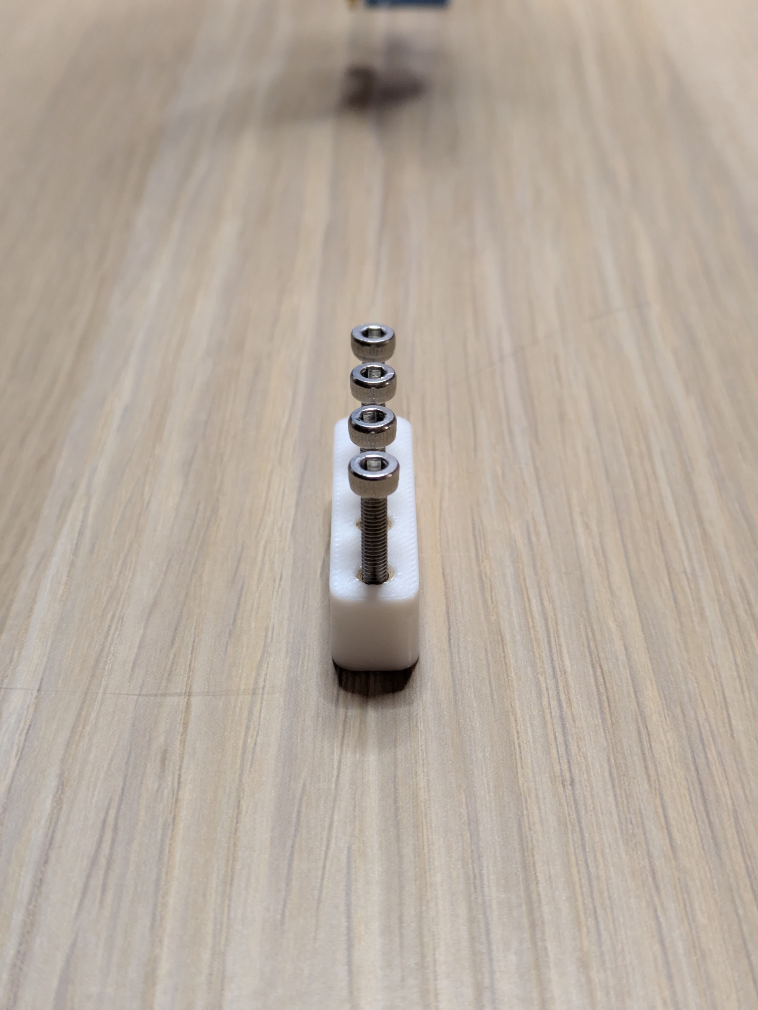 A photo of four silver bolts screwed into a similar 3D printed part. This time, the screws are basically perfectly in a line with no visible wobble.